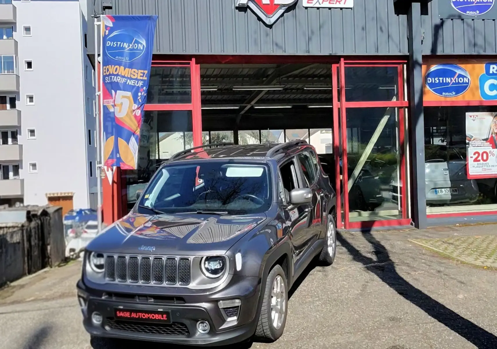 Jeep Renegade Granite Crystal métallisé en 3/4 avant droit, devant un garage avec enseigne AD Expert.