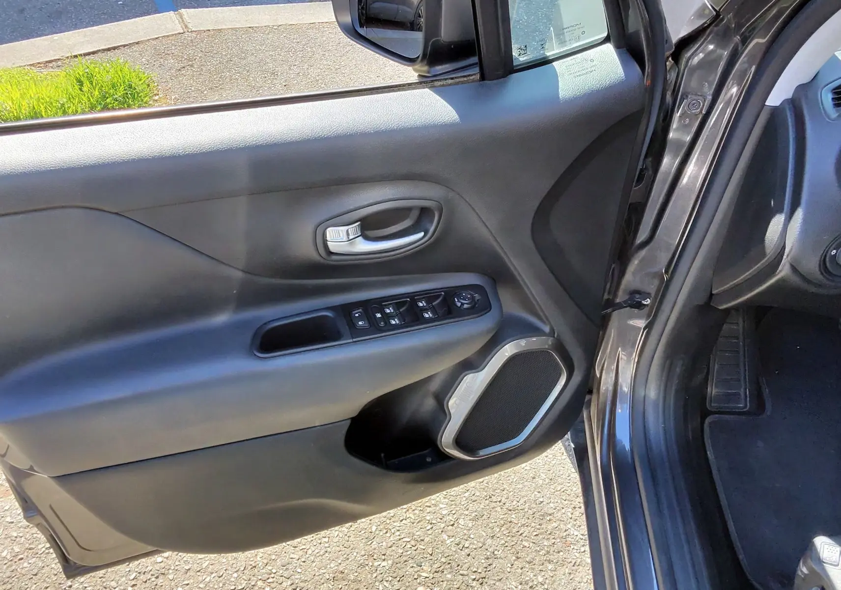 Vue rapprochée de la porte avant gauche ouverte d’un Jeep Renegade Granite Crystal 2020, avec commandes électriques et haut-parleur intégré.