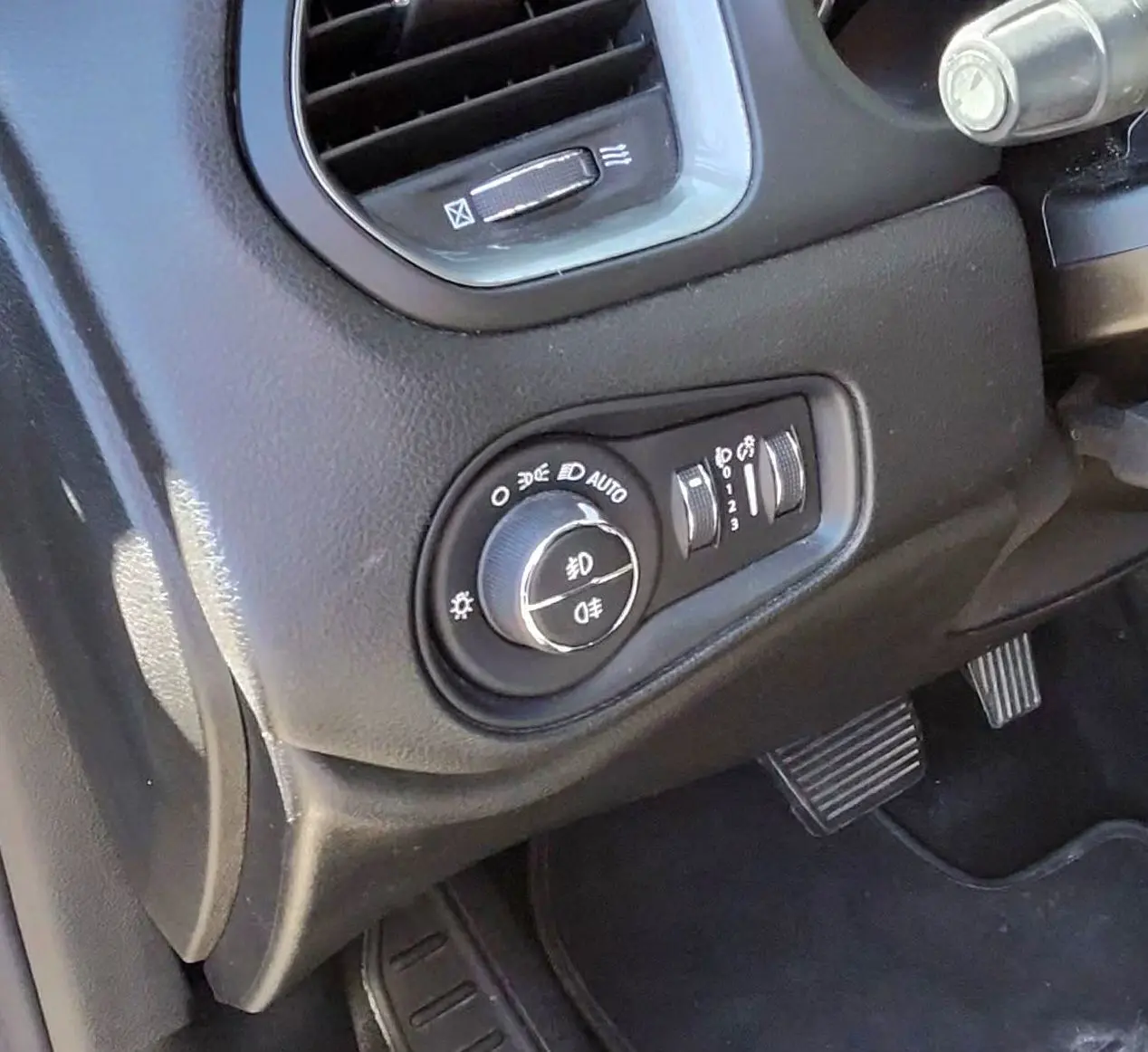 Gros plan sur le tableau de bord noir du Jeep Renegade 2020, montrant la commande des phares et les pédales.