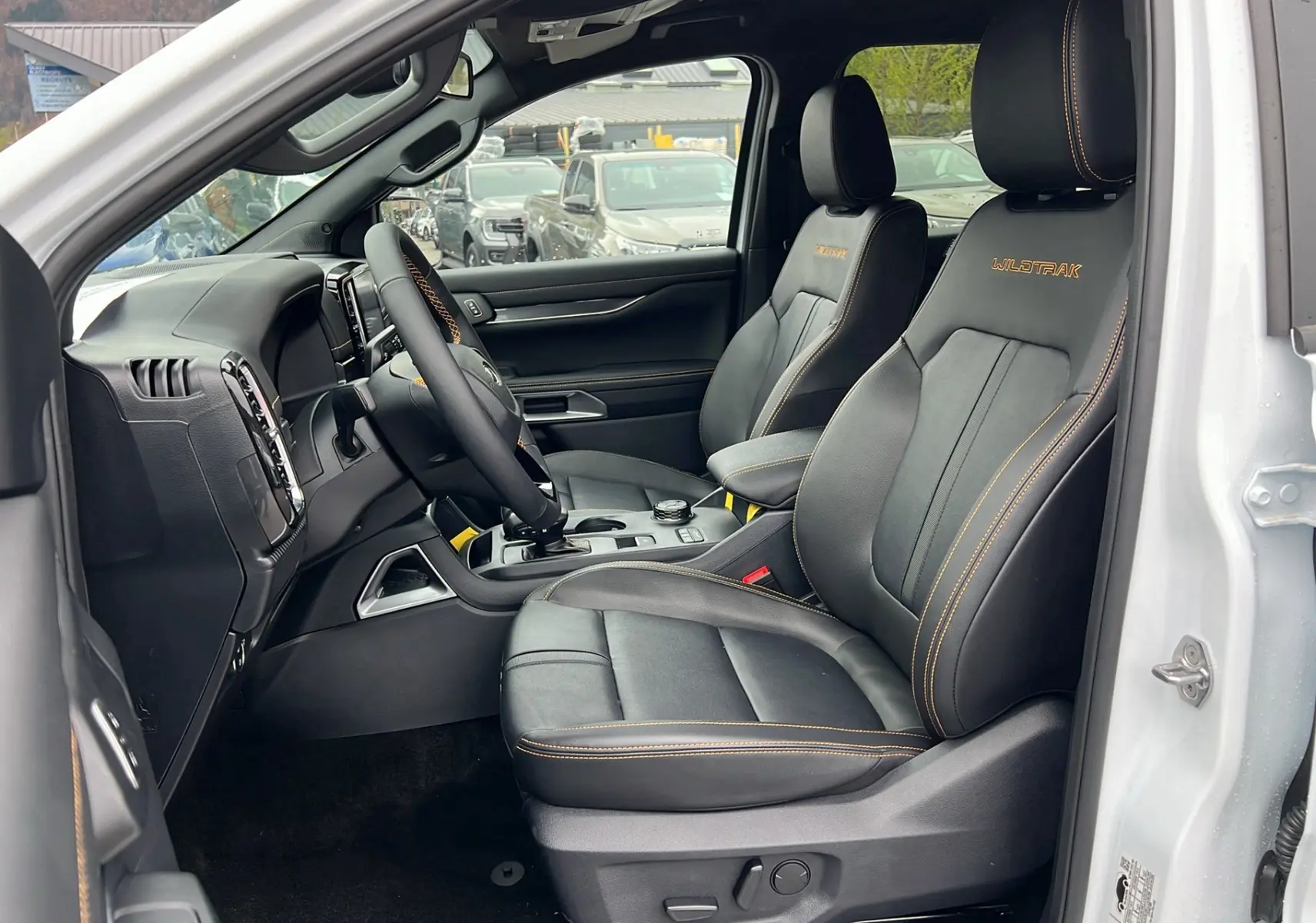 Vue intérieure côté conducteur du Ford Ranger 2025 blanc glacier, sièges cuir noirs avec surpiqûres orange Wildtrak.