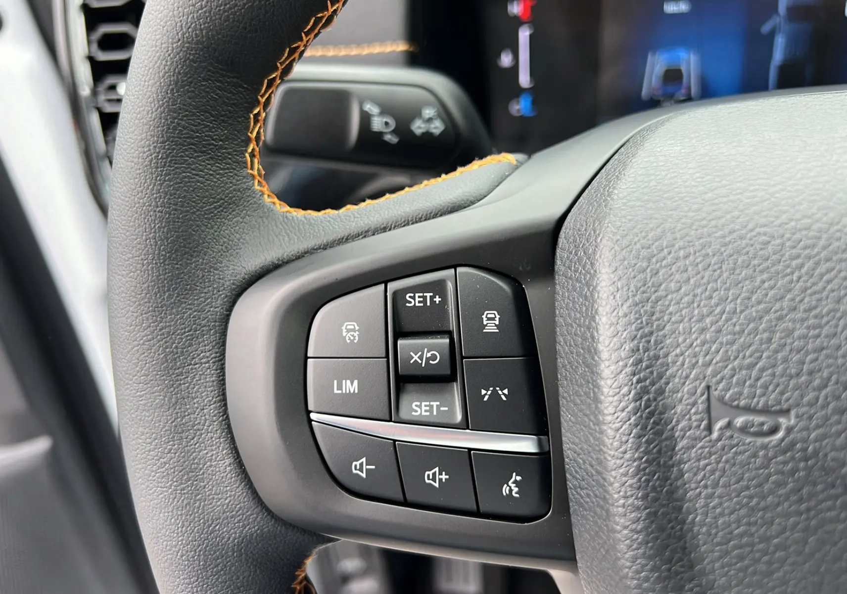 Gros plan sur les commandes multifonctions à gauche du volant cuir noir avec surpiqûres orange du Ford Ranger blanc glacier 2025.