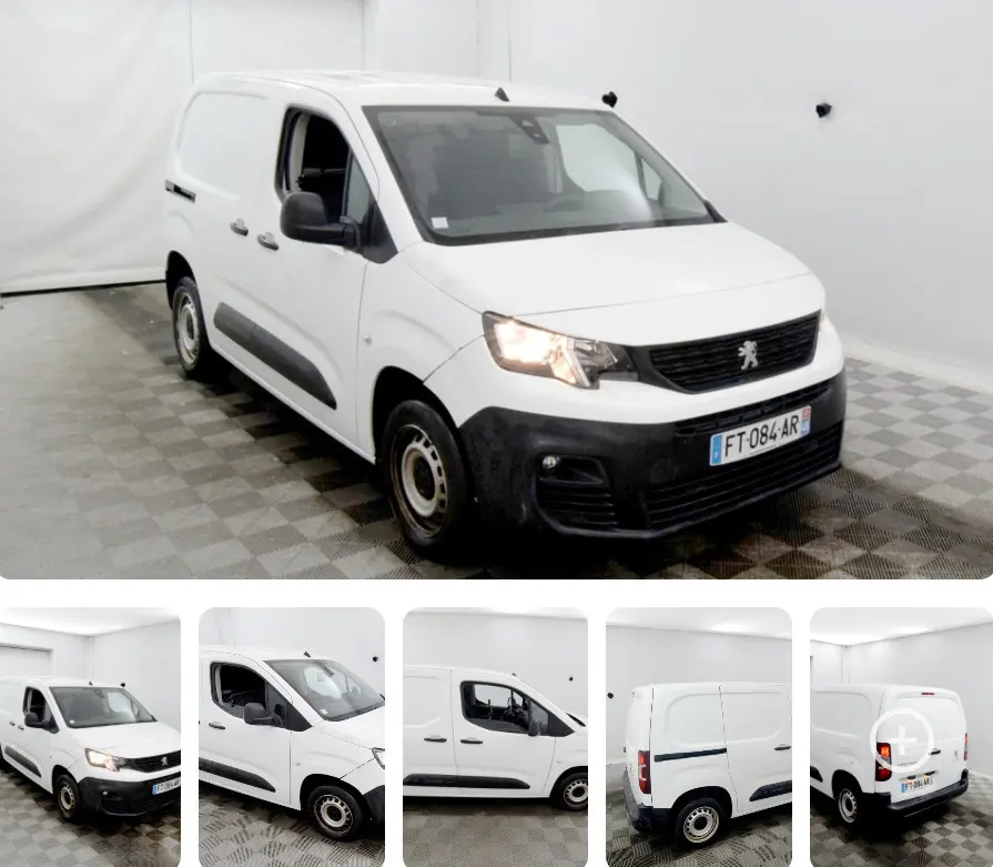 Peugeot Partner blanc vue 3/4 avant droit en intérieur, avec phares allumés et protections noires sur les portes.