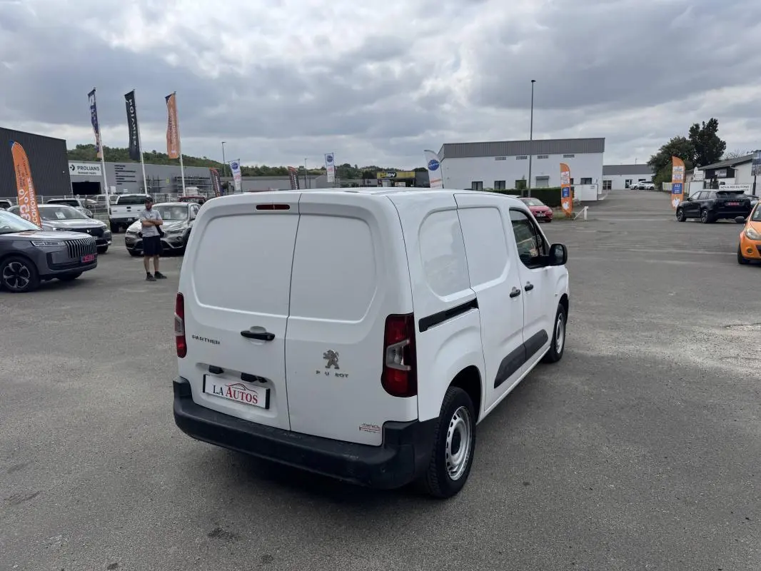 Vue 3/4 arrière droite d'un Peugeot Partner blanc 2020 utilitaire avec portes arrière battantes et protections latérales noires.
