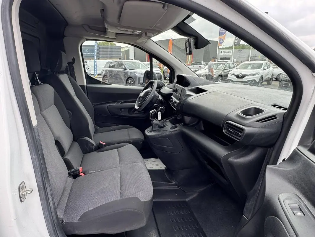 Vue intérieure côté conducteur du Peugeot Partner blanc 2020, montrant les sièges avant et le tableau de bord avec boîte manuelle.