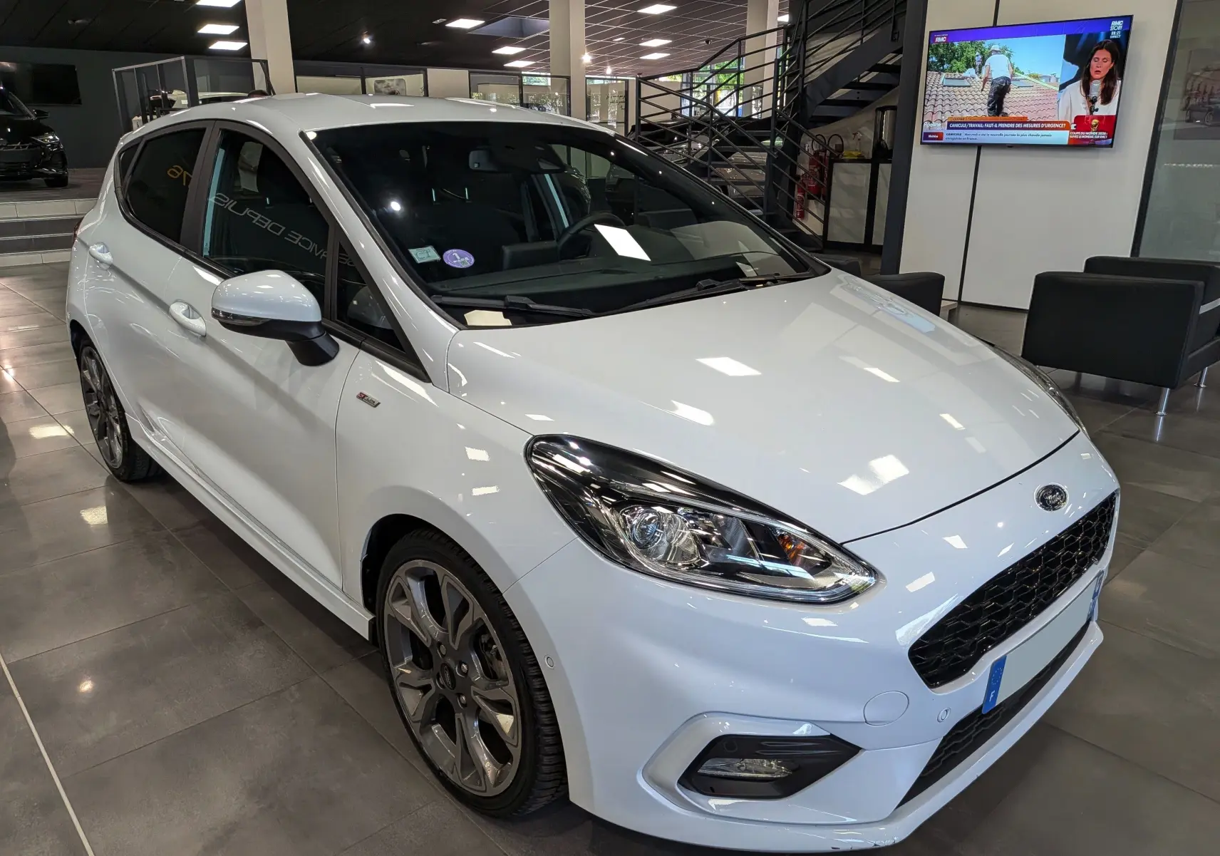 Ford Fiesta blanche vue en 3/4 avant droit dans un showroom, avec jantes alliage et phares LED distinctifs.