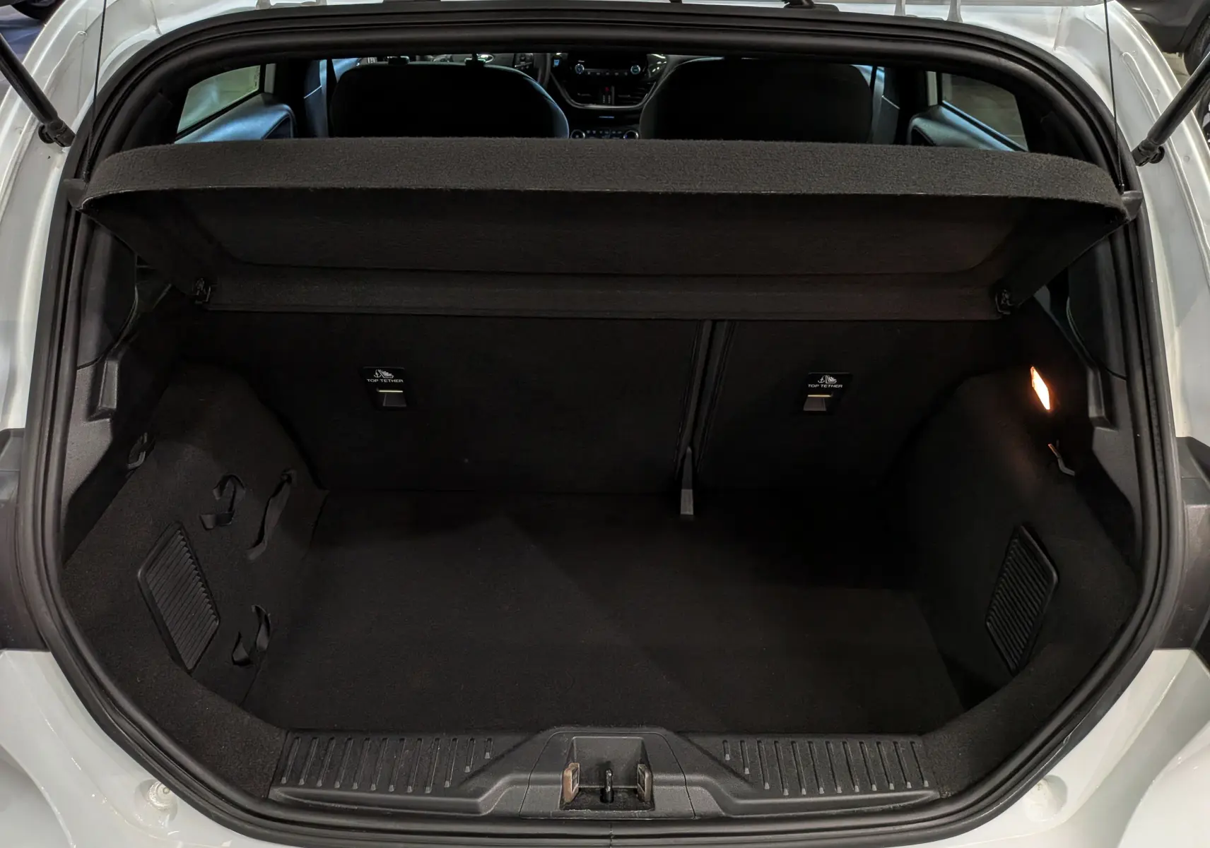 Vue arrière du coffre ouvert d'une Ford Fiesta blanche 2020, intérieur noir avec tablette de séparation relevée.