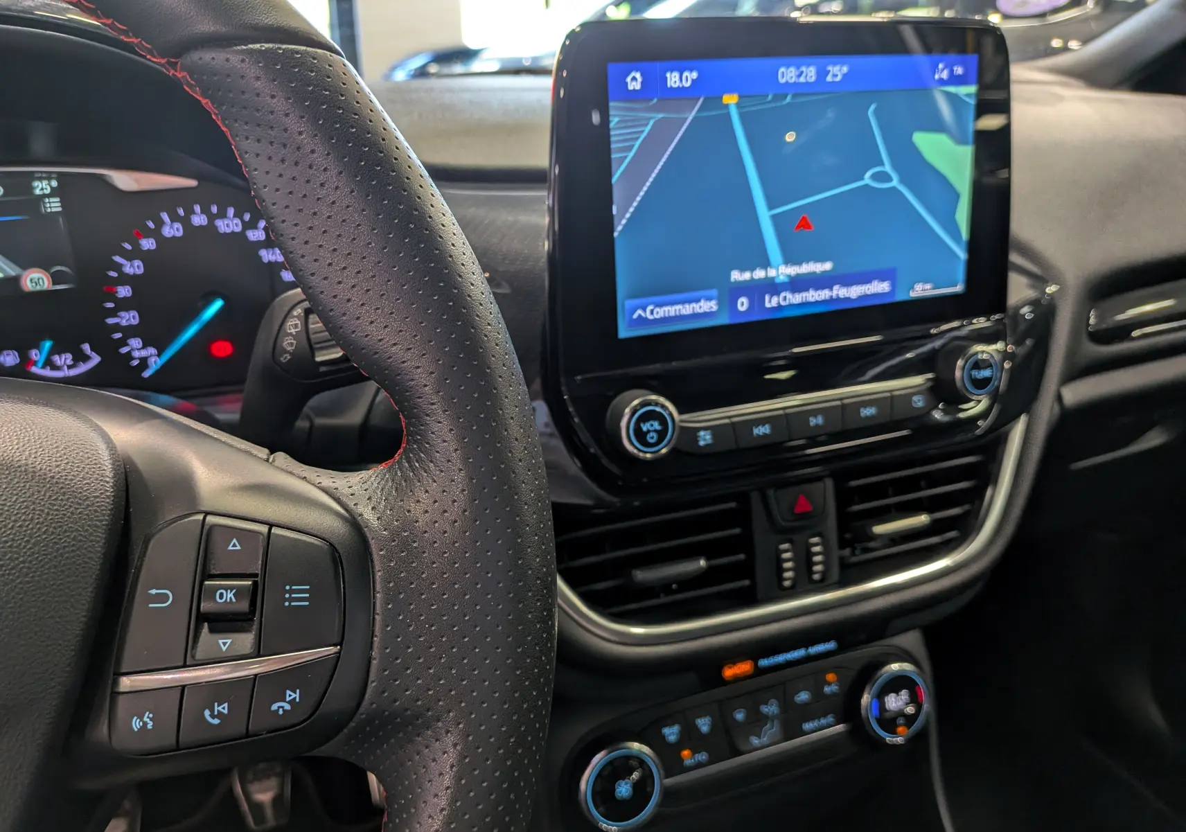 Vue rapprochée du tableau de bord et du volant perforé de la Ford Fiesta blanche avec écran tactile de navigation allumé.