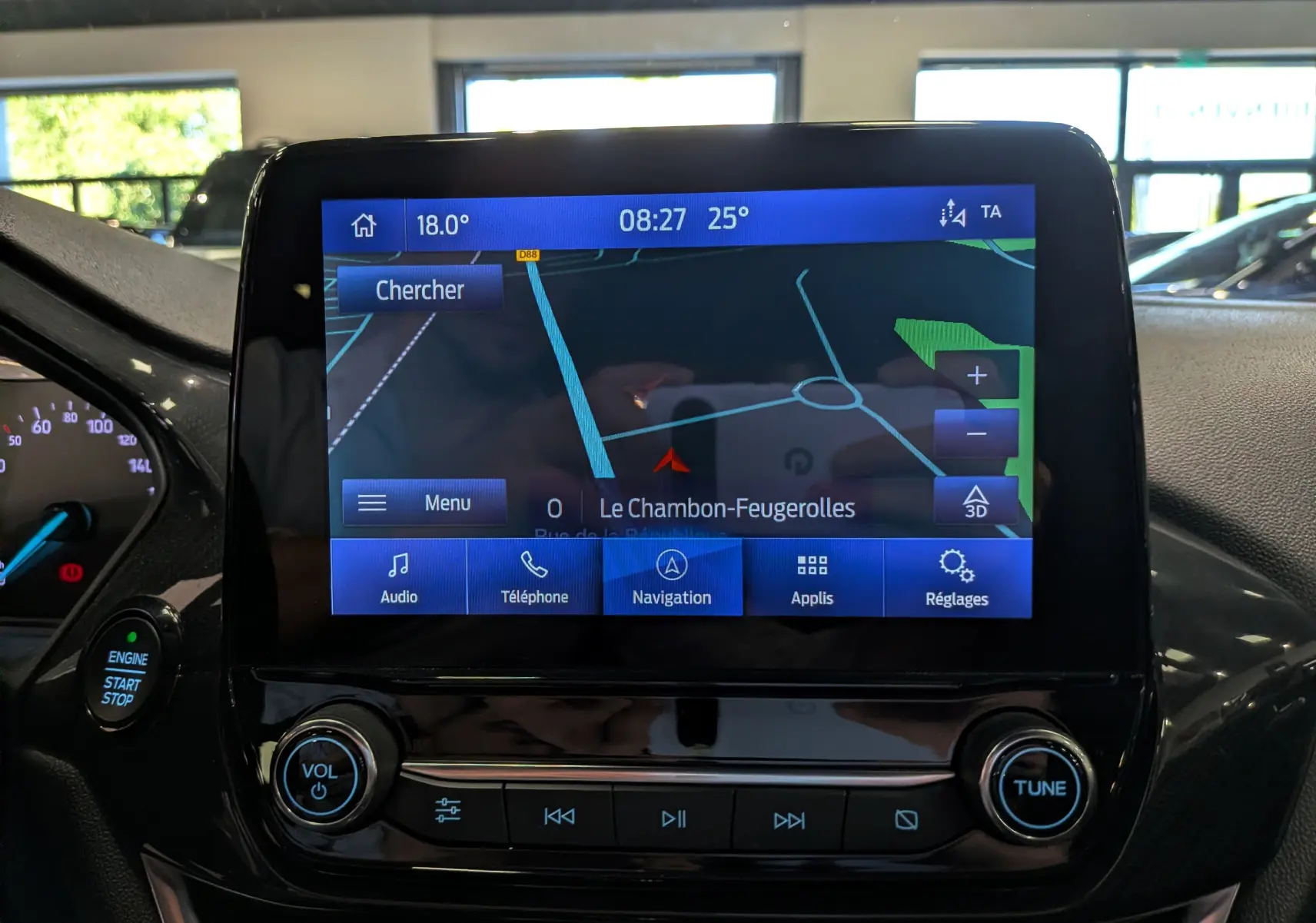 Vue rapprochée de l’écran tactile central de la Ford Fiesta blanche, affichant la navigation avec commandes audio et téléphone.