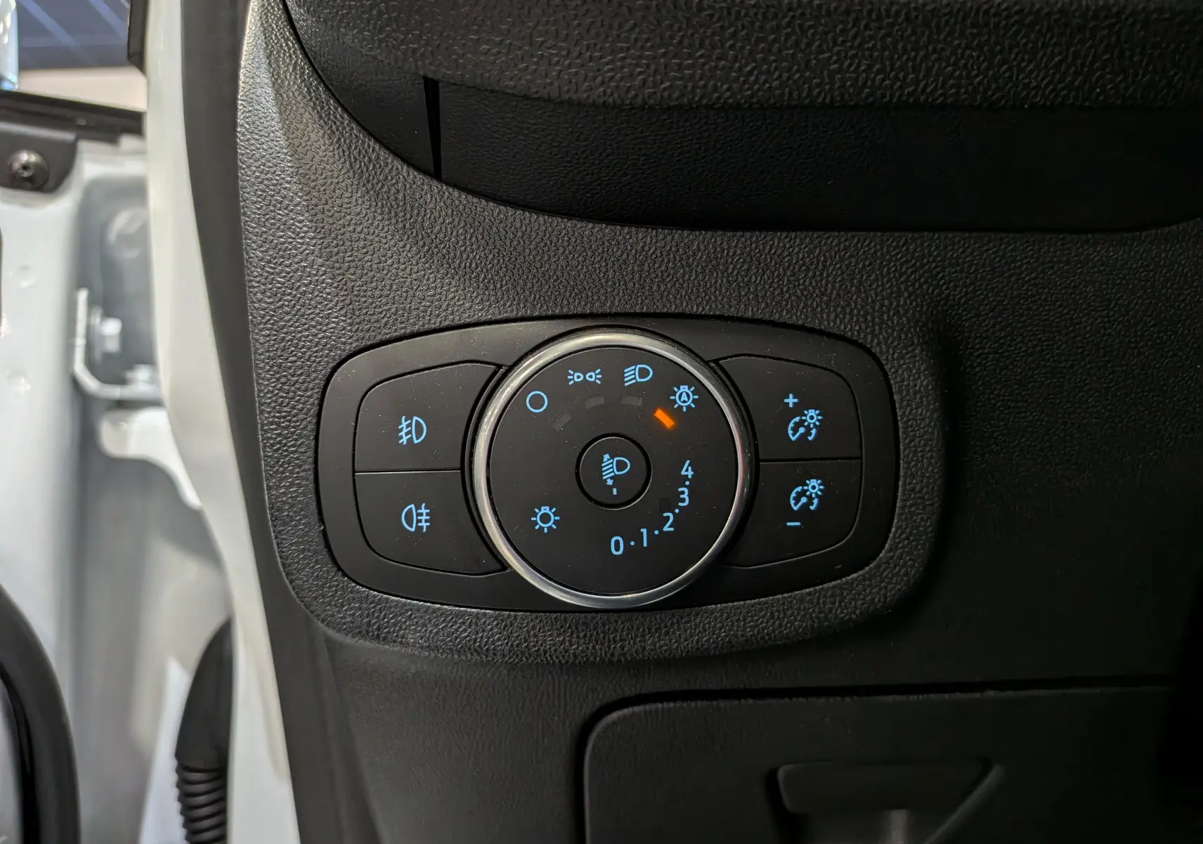 Gros plan sur le panneau de commande des phares et réglages lumineux à gauche du tableau de bord d'une Ford Fiesta blanche 2020.