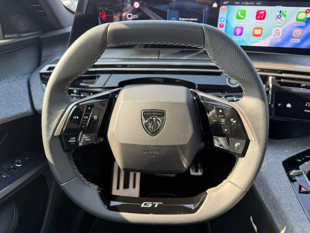 Vue rapprochée du volant gris perforé du Peugeot 3008 Hybrid 145 e-DCS6 GT avec commandes intégrées et logo central.