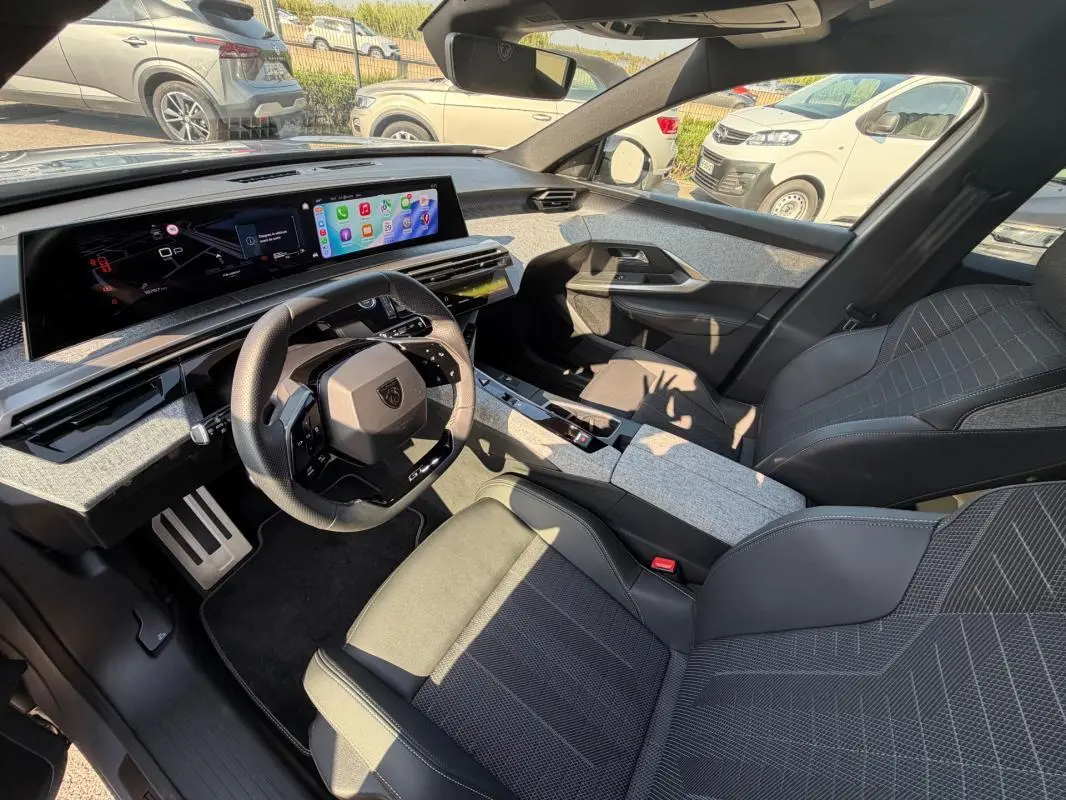 Intérieur du Peugeot 3008 Hybrid 2025 vu côté conducteur, avec tableau de bord numérique et sellerie gris foncé.