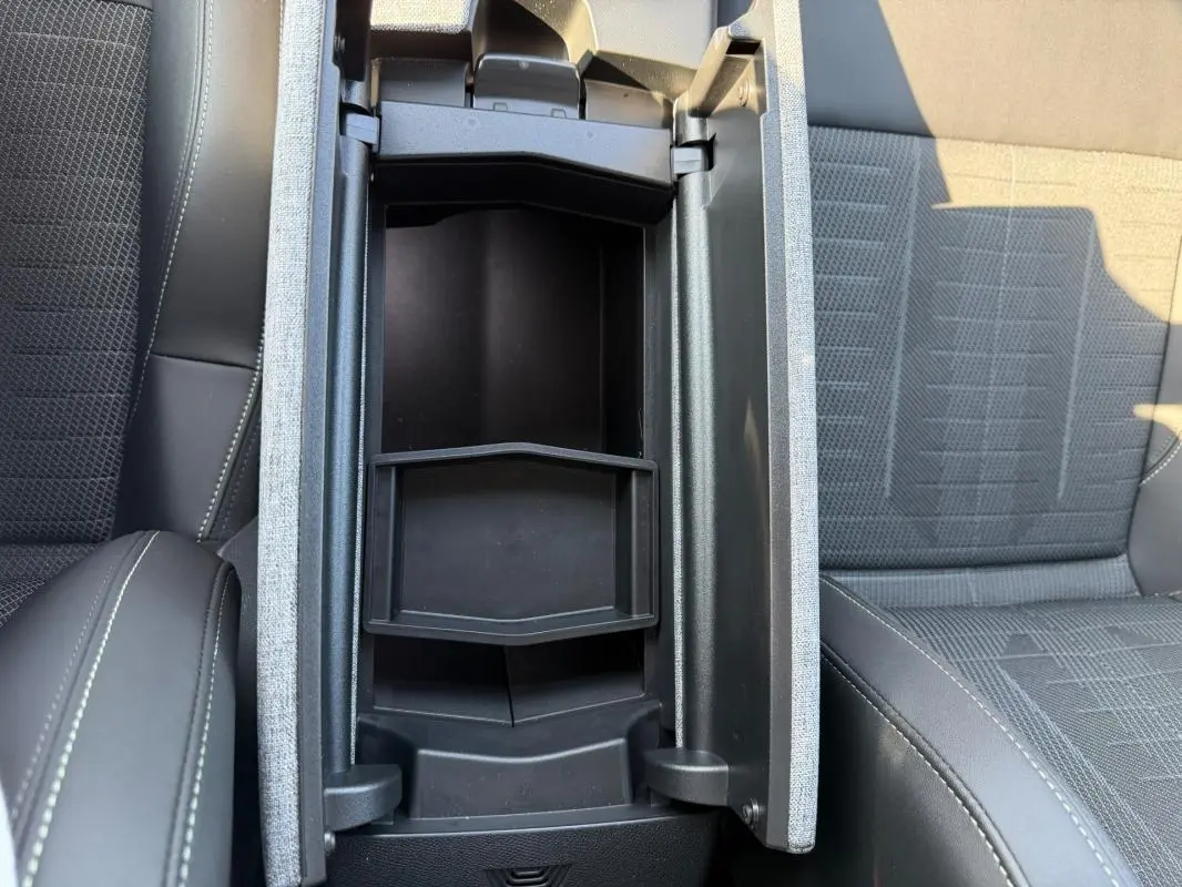 Vue plongeante sur l'accoudoir central ouvert entre les sièges tissu gris et cuir noir du Peugeot 3008 Hybrid 145 e-DCS6 GT 2025.
