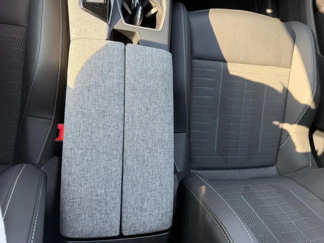 Vue rapprochée de l’accoudoir central gris et des sièges en tissu noir du Peugeot 3008 Hybrid 145 e-DCS6 GT 2025.