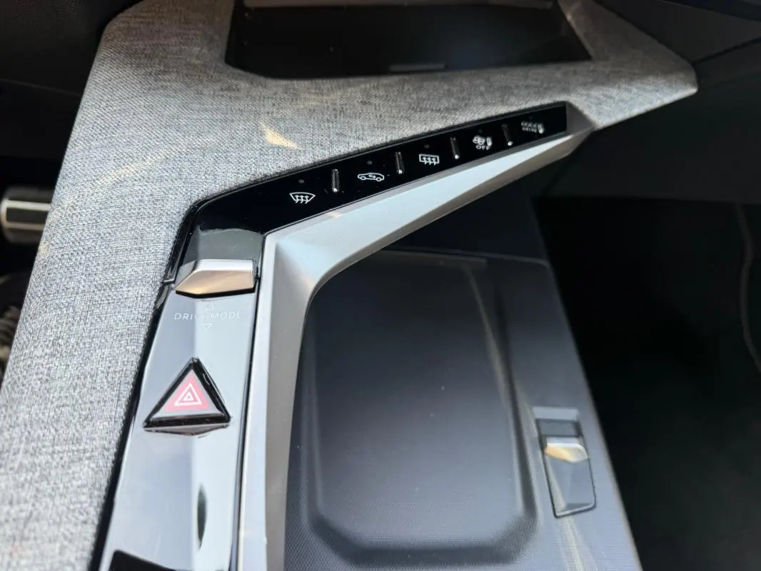 Gros plan sur la console centrale grise du Peugeot 3008 Hybrid 145 e-DCS6 GT 2025 avec boutons de commande et tissu texturé.