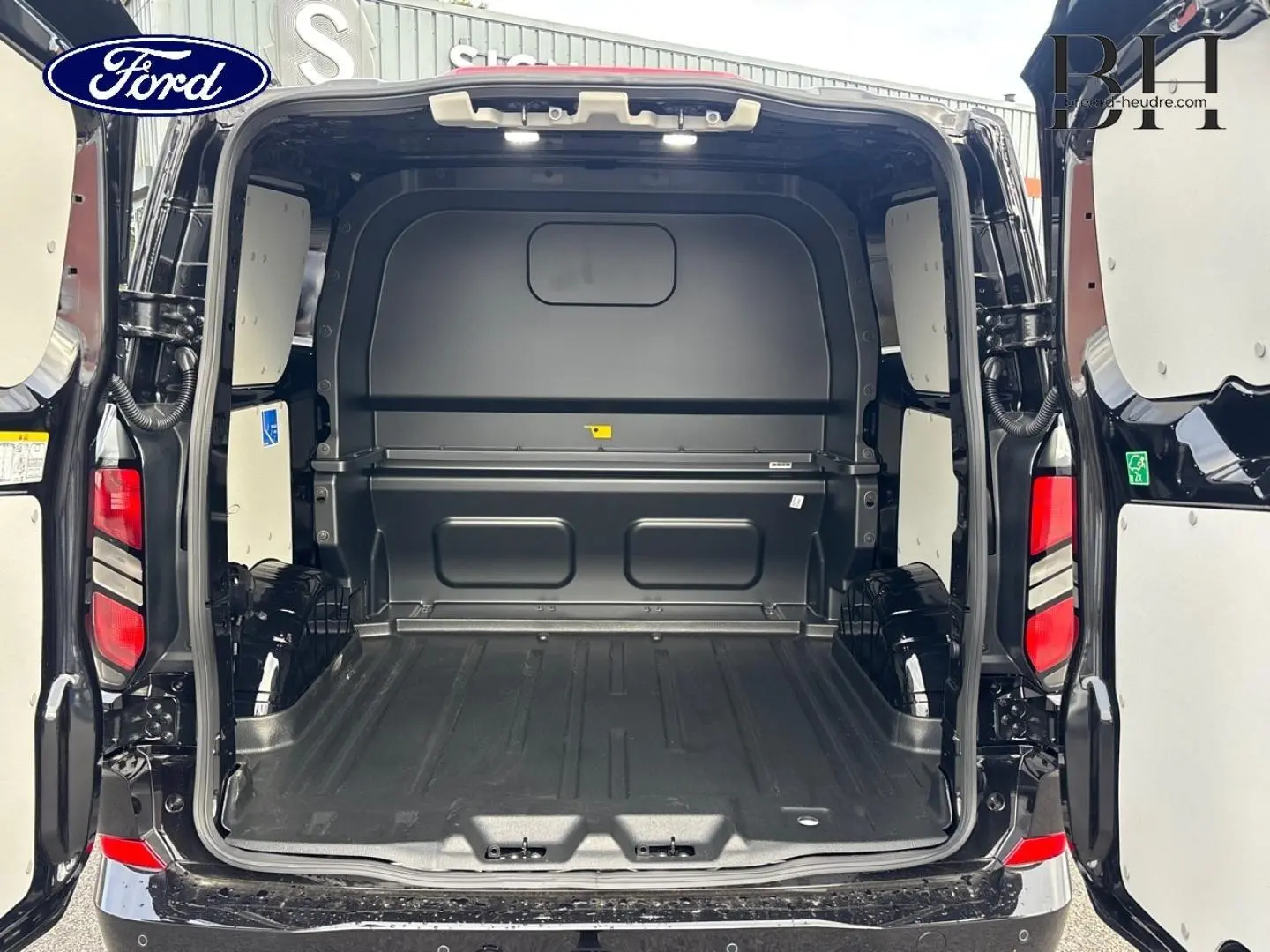 Vue arrière du fourgon Ford Transit Custom noir Agate Métallisée avec portes ouvertes montrant l’espace de chargement vide.