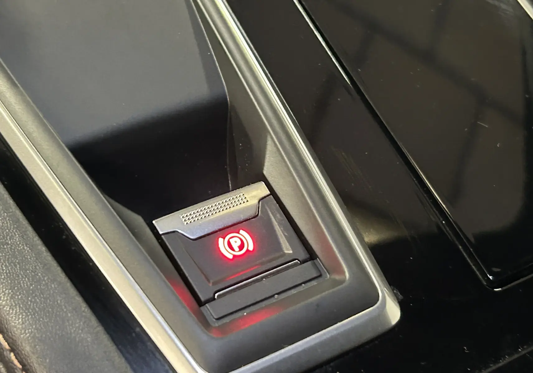 Gros plan sur le bouton de frein à main électronique rouge dans la console centrale d'une Peugeot 508 SW gris Selenium 2024.