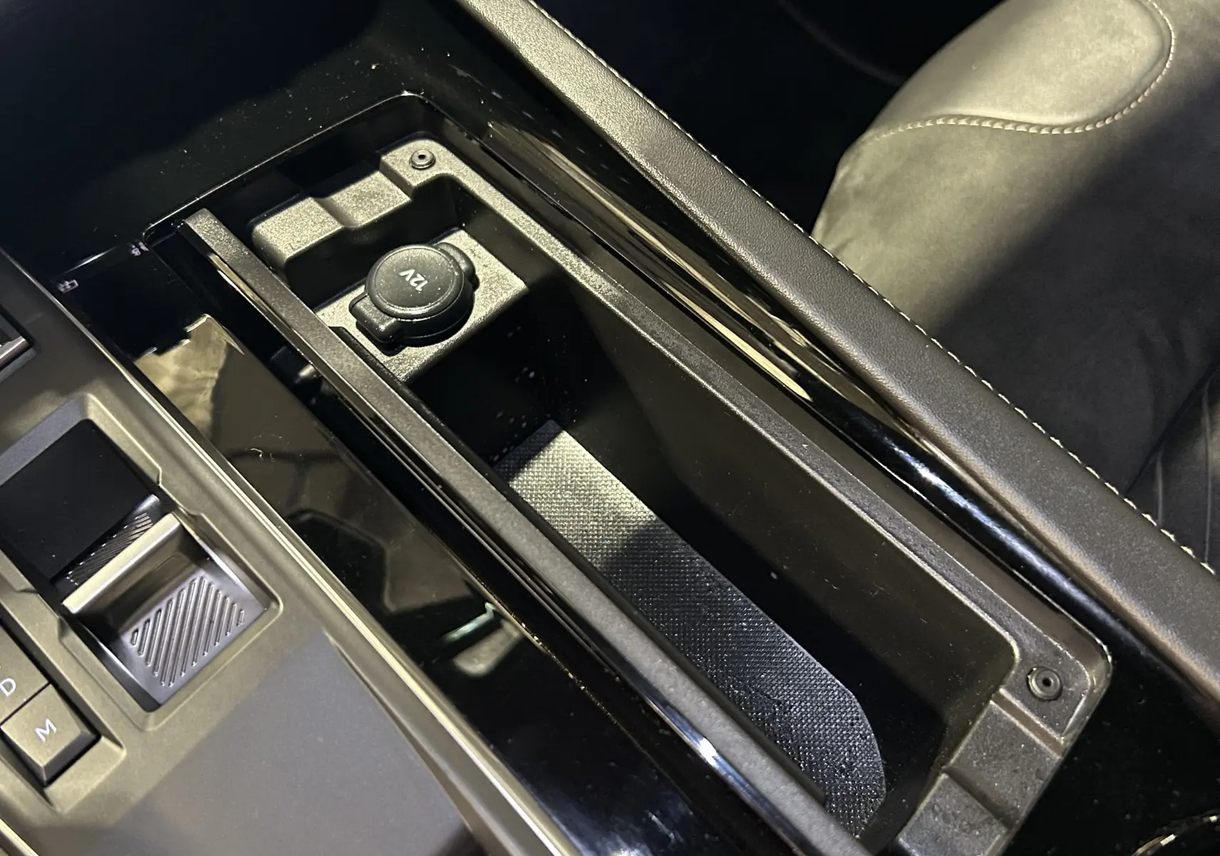 Gros plan sur la console centrale noire et prise 12V du Peugeot 508 SW II Ph.2 BlueHDi 130 EAT8 GT, intérieur cuir gris.