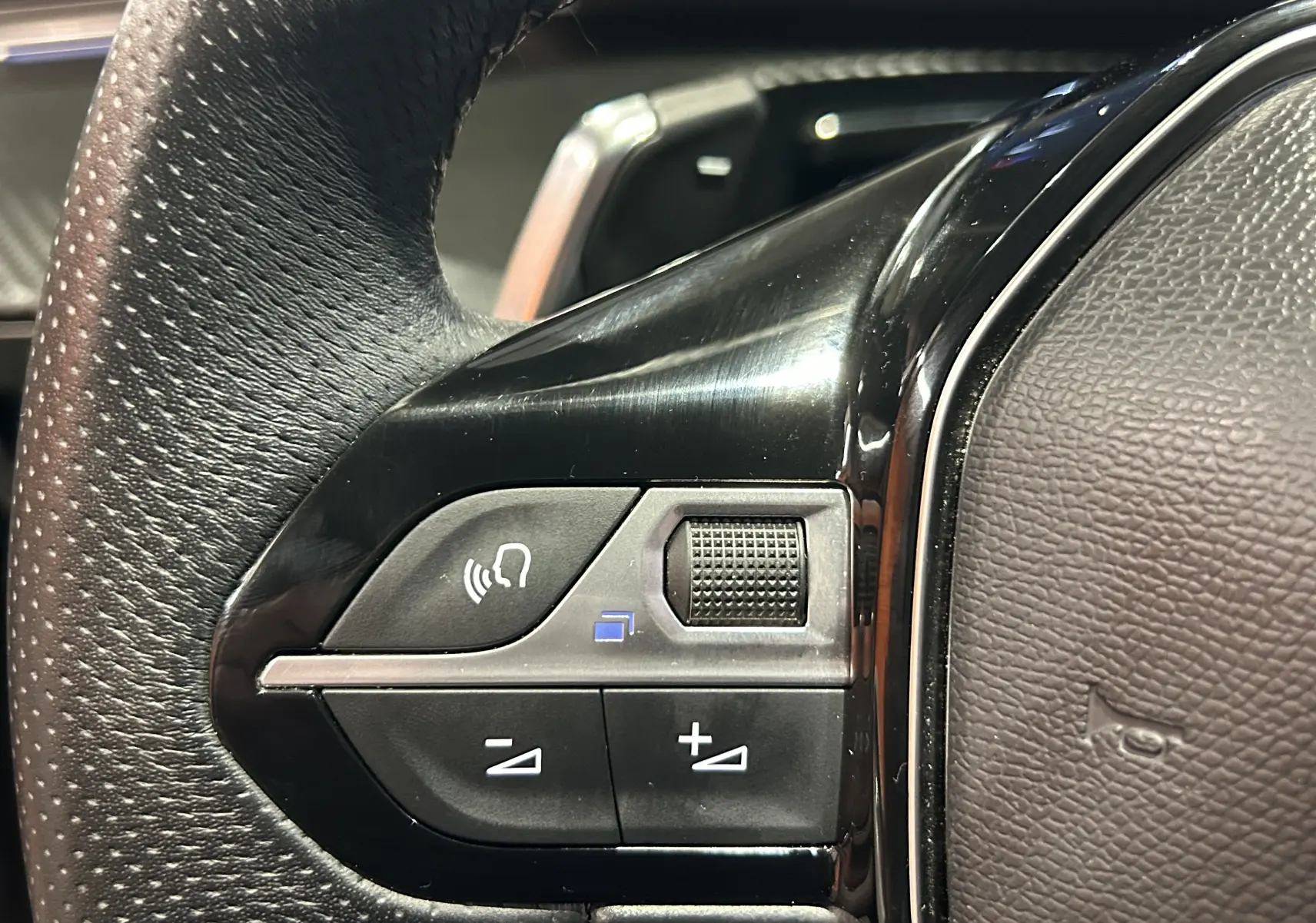 Gros plan sur les commandes gauche du volant cuir noir du Peugeot 508 SW Gris Selenium 2024 avec molette et boutons de volume.