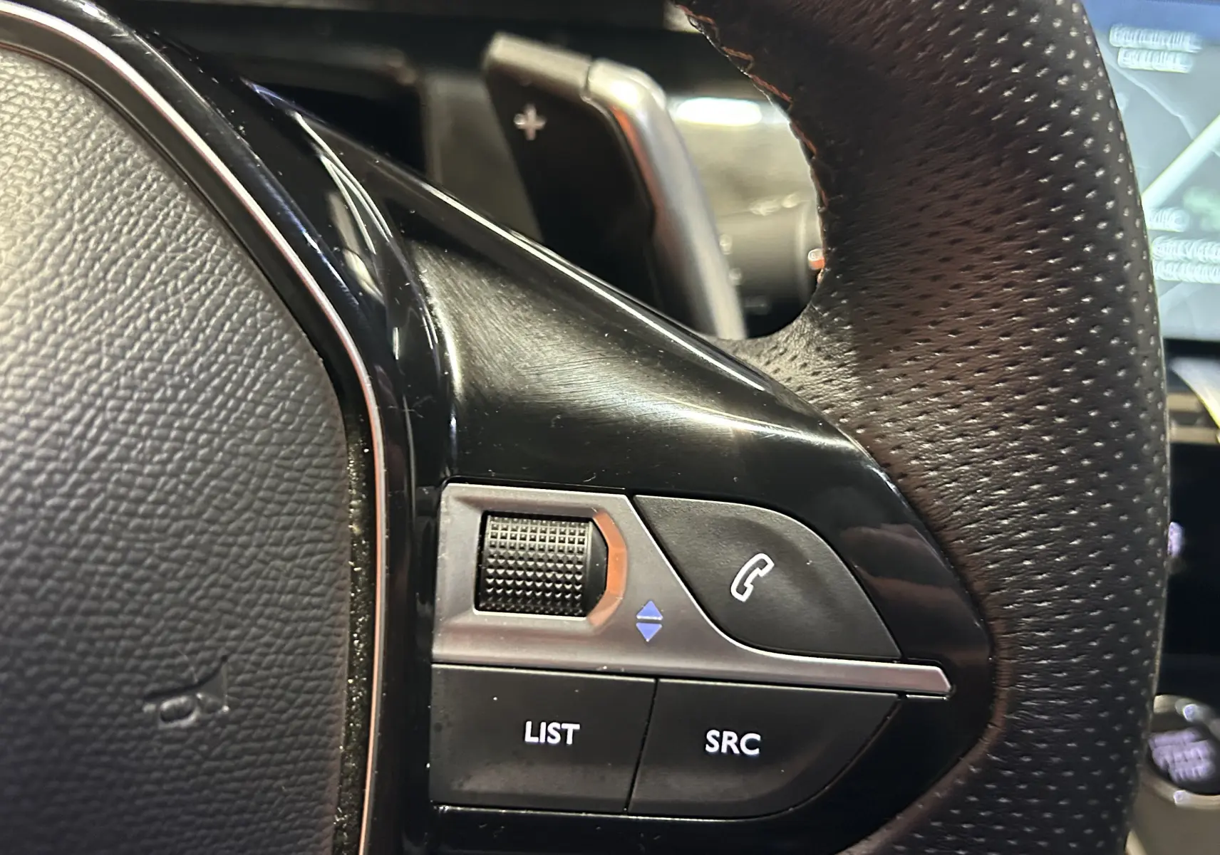 Gros plan sur les commandes gauche du volant en cuir perforé du Peugeot 508 SW 2024 gris Selenium.