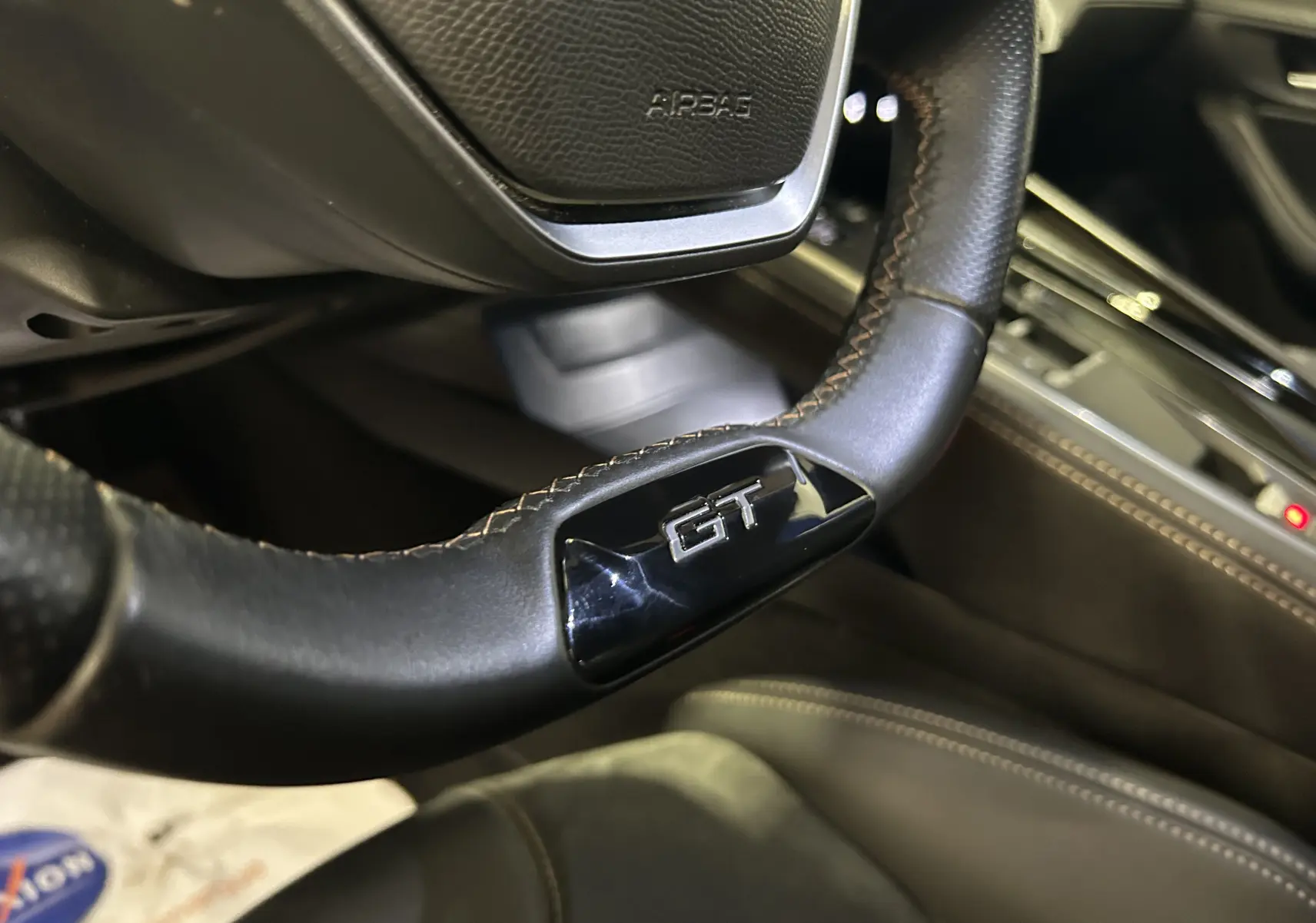 Gros plan sur le volant cuir noir embossé GT de la Peugeot 508 SW 2024, avec coutures apparentes et tableau de bord partiel.