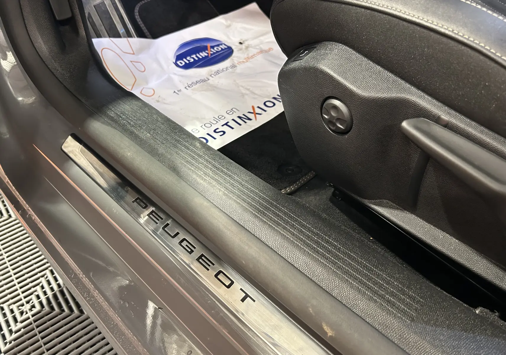 Gros plan sur la plaque de seuil de porte Peugeot gris Selenium côté conducteur avec siège en cuir noir et tapis Distinxion.