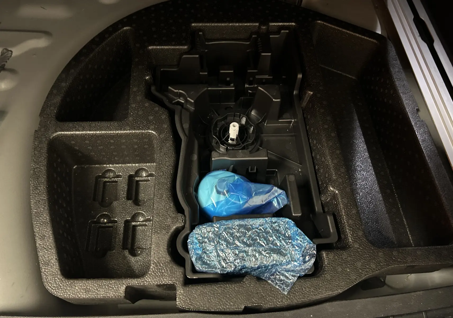 Rangement en mousse noire sous le coffre du Peugeot 508 SW 2024 avec accessoires emballés en plastique bleu.