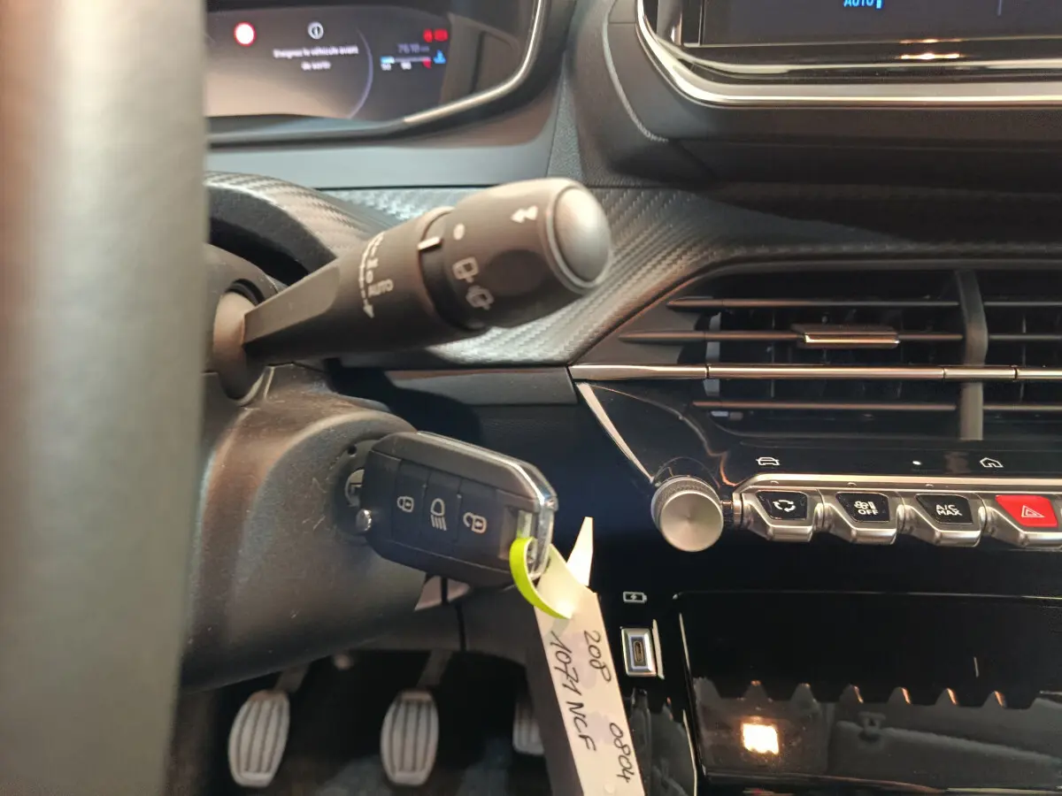 Gros plan sur le tableau de bord et la clé insérée à gauche du volant d'une Peugeot 208 gris clair, version 2025.