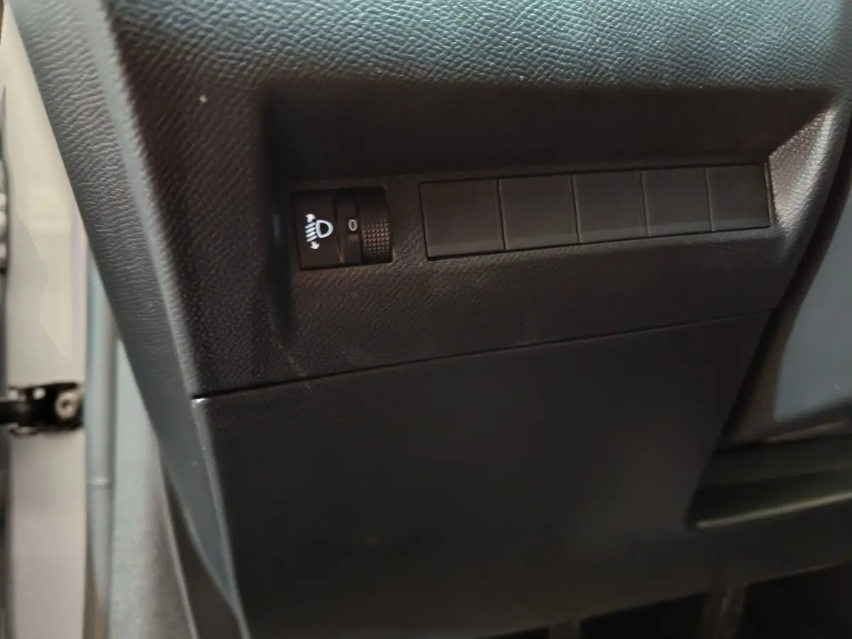 Gros plan sur le tableau de bord côté conducteur de la Peugeot 208 gris clair, montrant la molette de réglage des phares.