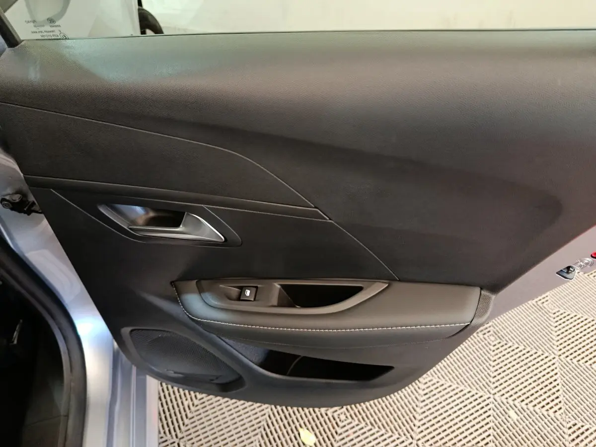 Vue rapprochée de la porte avant gauche gris clair de la Peugeot 208 PureTech 100 S&S Allure avec poignée et commande de vitre.