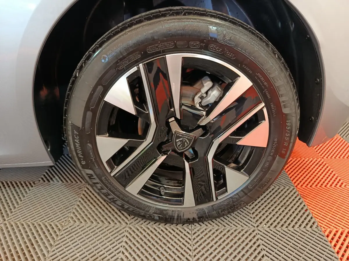 Gros plan sur la roue avant gauche gris clair de la Peugeot 208 avec jante alliage noire et argentée au design moderne.