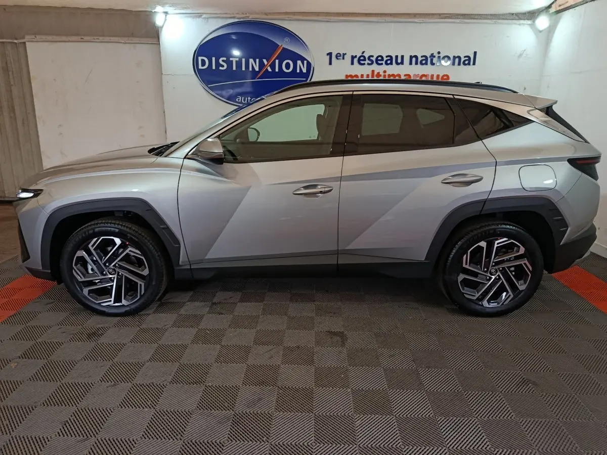 Vue de profil côté gauche d'un Hyundai Tucson gris clair 2025 avec jantes alliage et lignes anguleuses marquées.