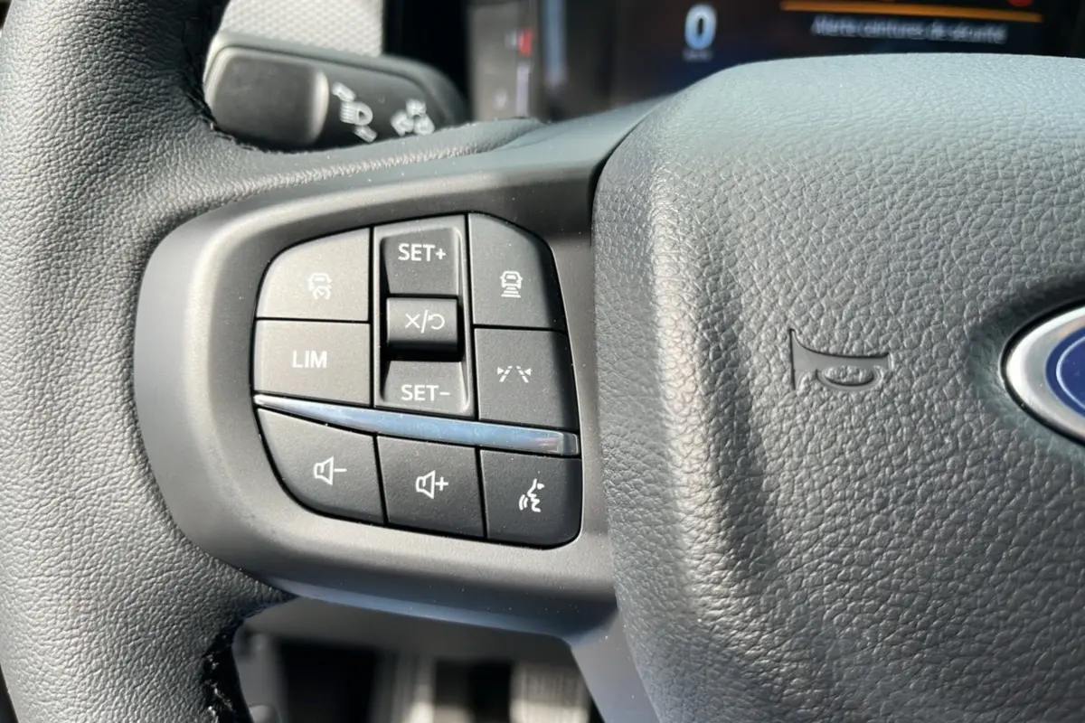 Gros plan sur les commandes de régulateur et volume au volant cuir noir du Ford Ranger gris carbone 2025.