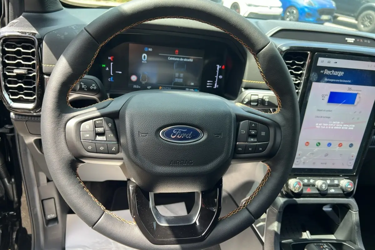 Vue rapprochée du volant cuir noir avec surpiqûres jaunes du Ford Ranger 2026, tableau de bord et écran tactile visibles.