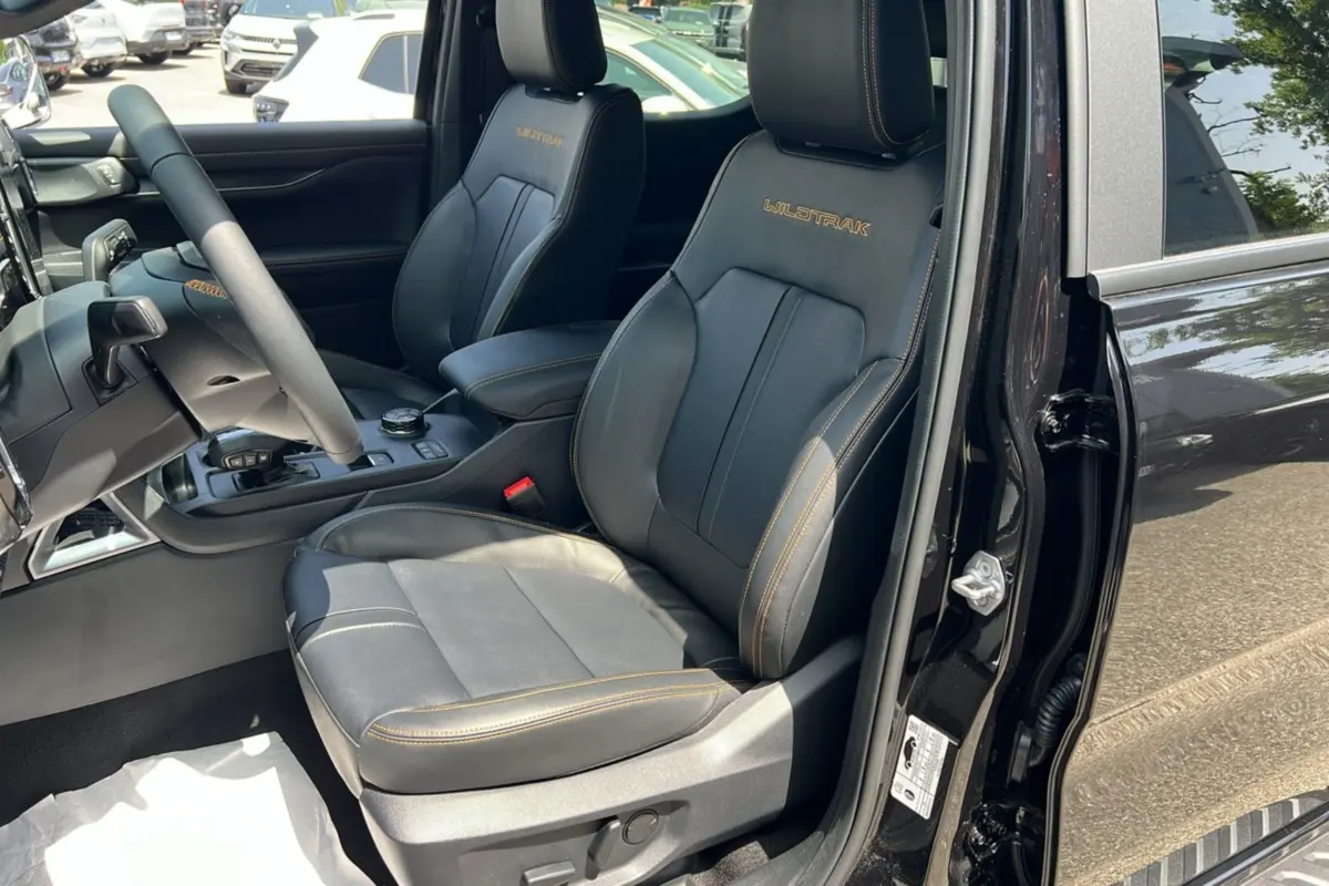 Vue intérieure côté conducteur du Ford Ranger Wildtrak noir agate, sièges cuir avec surpiqûres orange et logo brodé Wildtrak.