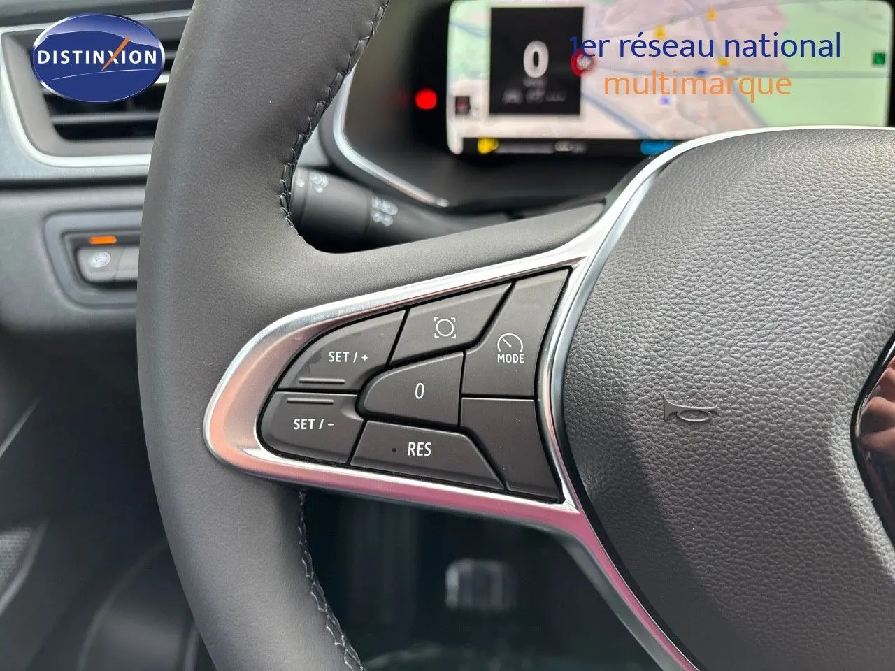 Gros plan sur les commandes à gauche du volant gris cuir du Renault Captur II hybride, tableau de bord numérique en arrière-plan.
