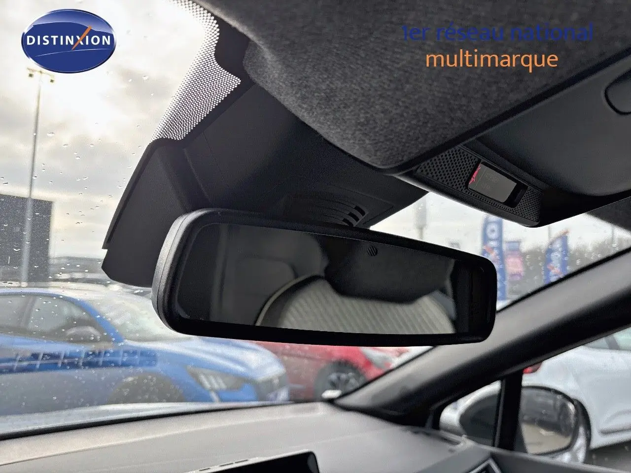 Vue intérieure du rétroviseur central d’un Renault Captur gris rafale métal avec toit noir, sous pluie légère en concession.