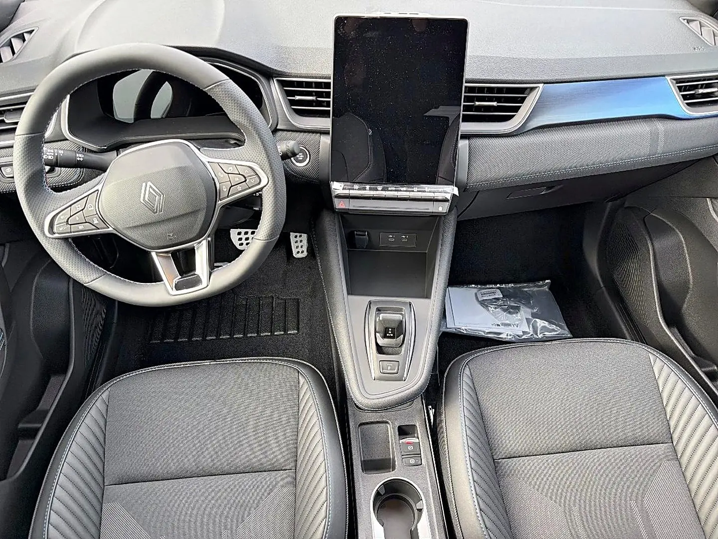 Vue intérieure avant du Renault Symbioz gris rafale, avec volant multifonction, écran tactile vertical et sièges tissu gris.