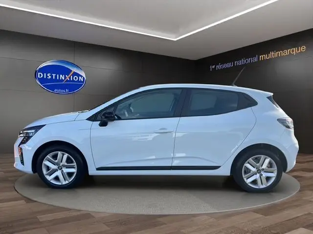 Profil côté gauche d'une Renault Clio V blanche 2025 sur fond intérieur avec jantes alliage 16 pouces et vitres teintées.