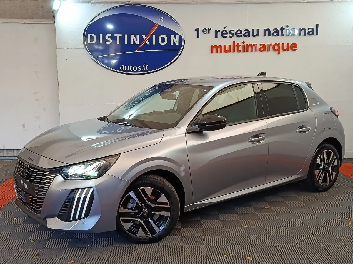 Peugeot 208 gris clair vue 3/4 avant droit, avec feux LED et jantes alliage noires distinctives.