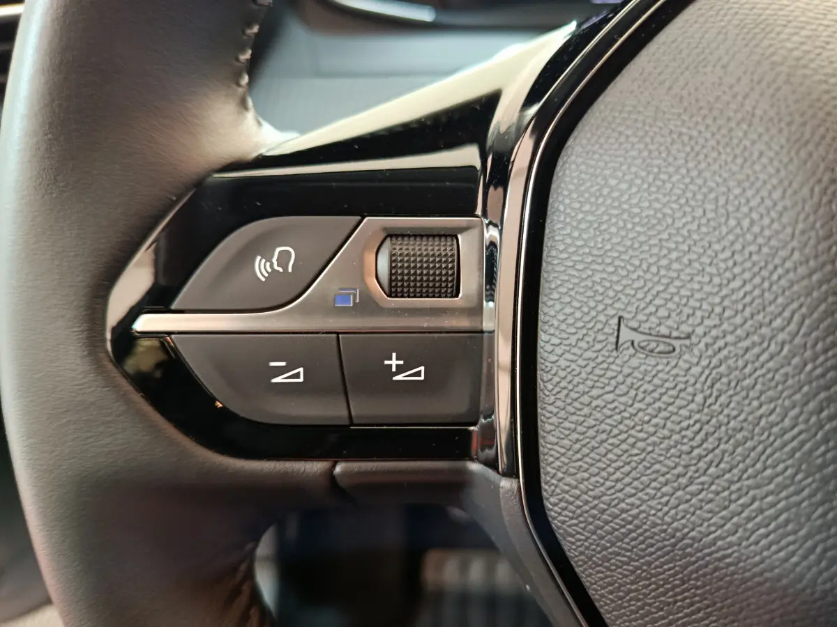 Gros plan sur les commandes gauche du volant cuir de la Peugeot 208 gris clair PureTech 100 S&S Allure 2025