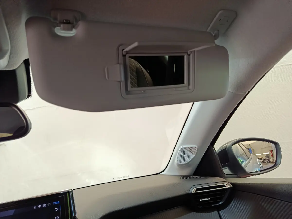 Intérieur de la Peugeot 208 gris clair, vue du pare-soleil avec miroir et rétroviseur côté droit visible.