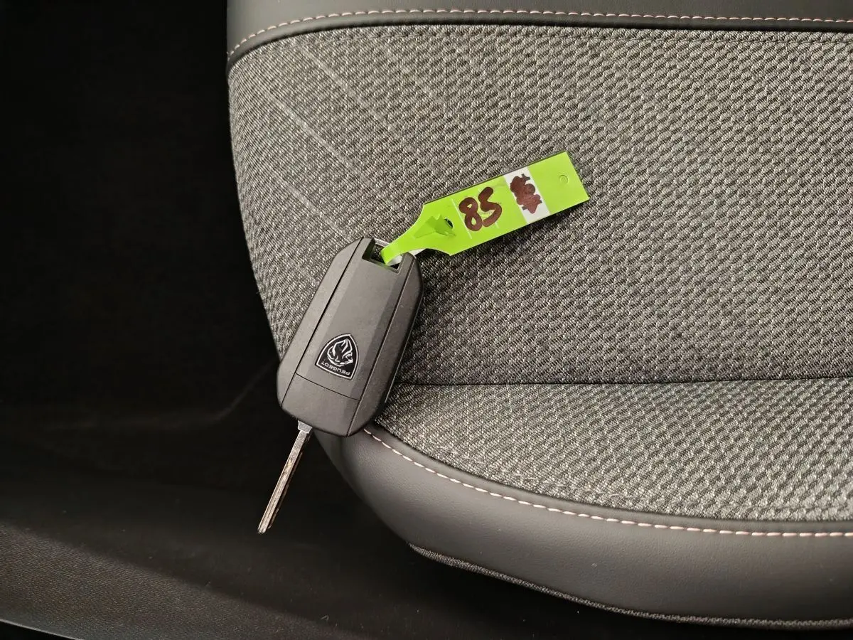 Clé Peugeot posée sur un siège avant gris clair en tissu avec surpiqûres contrastantes, vue rapprochée intérieure.
