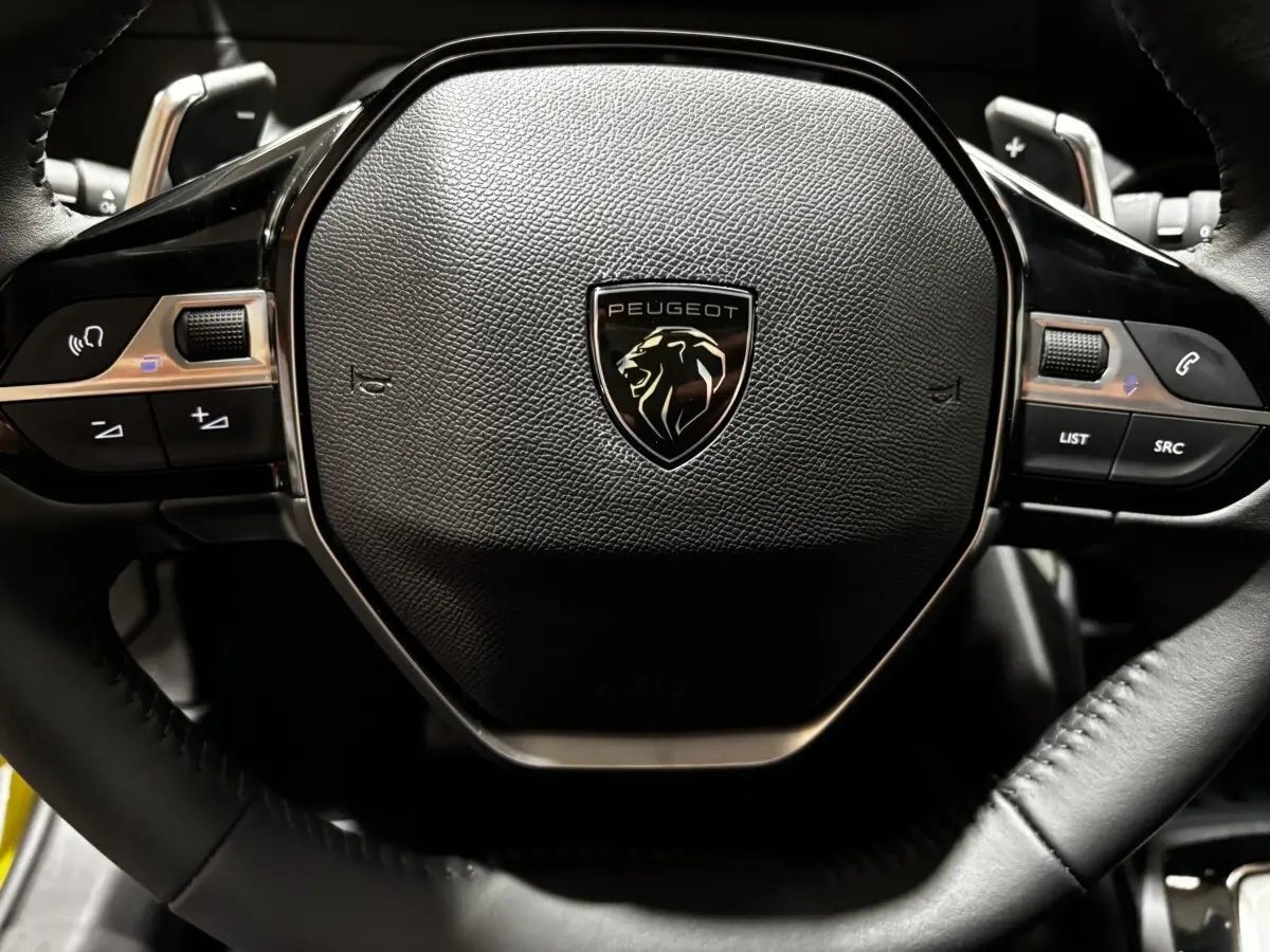 Gros plan sur le volant noir de la Peugeot 208 Hybrid 110 e-DCS6 Style avec logo lion central.