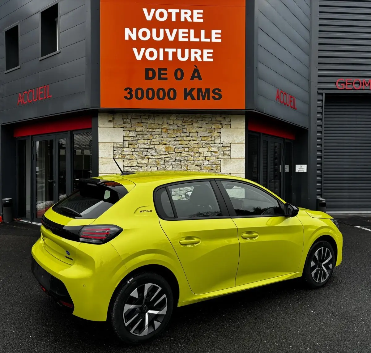 Vue 3/4 arrière droite d'une Peugeot 208 Hybrid jaune vif, finition Style, stationnée devant un bâtiment avec panneau orange.