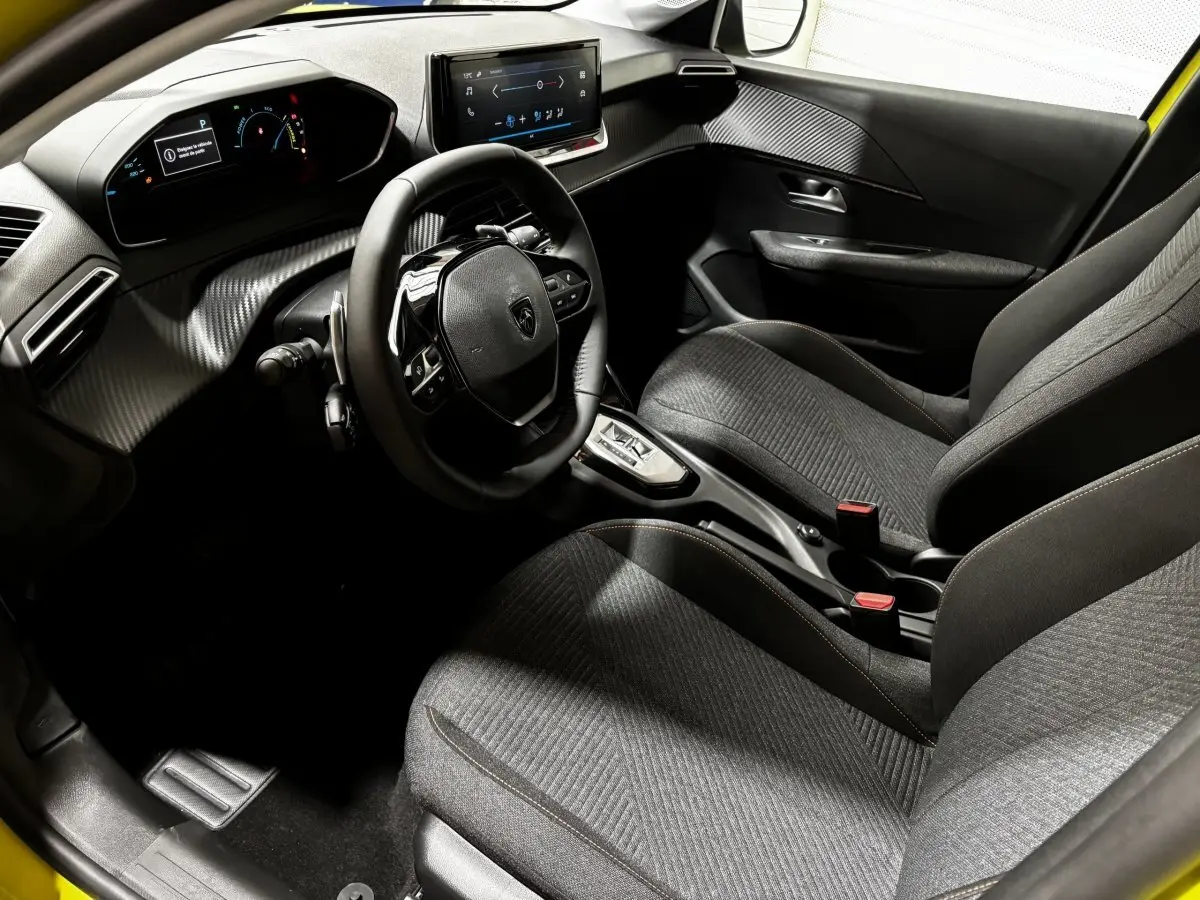 Vue intérieure côté conducteur de la Peugeot 208 Hybrid jaune, avec tableau de bord numérique et écran tactile central.