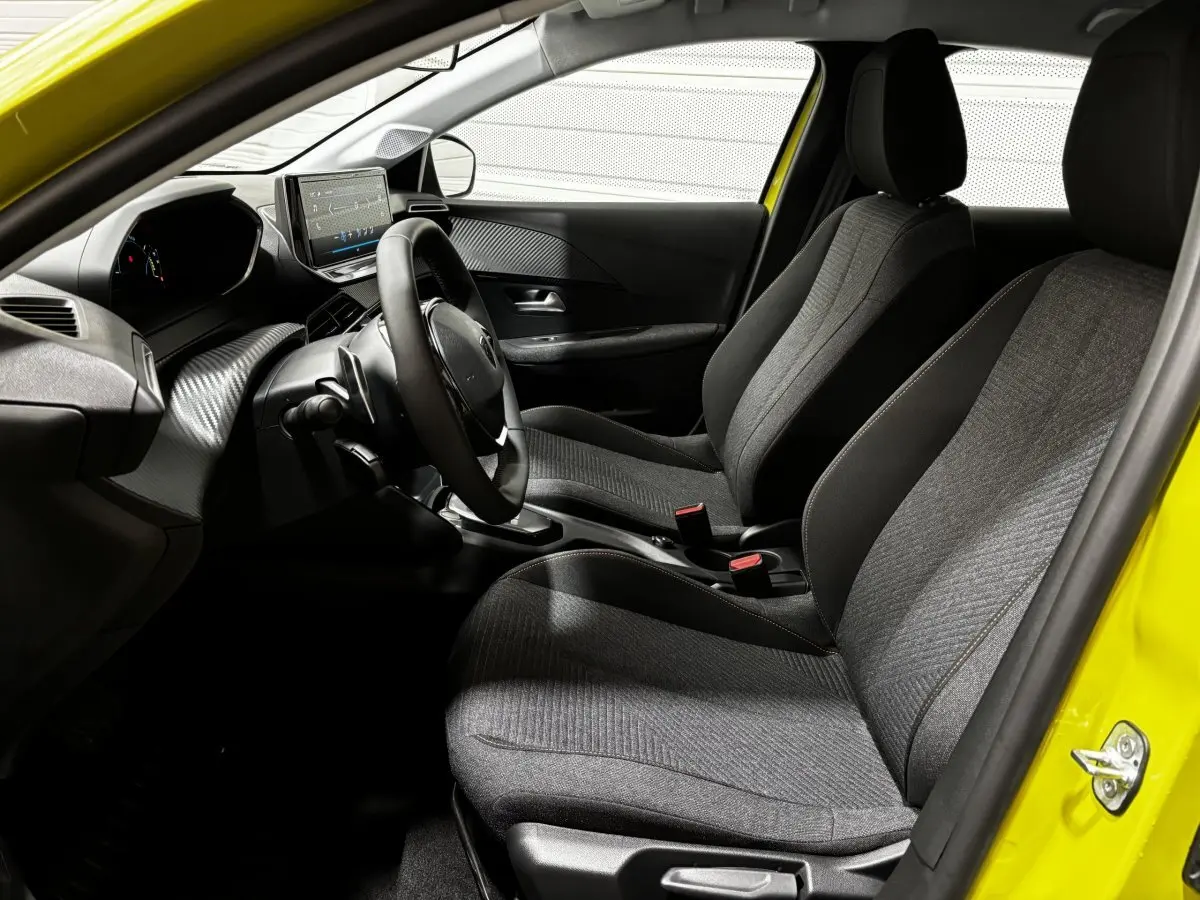Intérieur avant droit de la Peugeot 208 Hybrid jaune 2025, sièges gris et tableau de bord avec écran tactile central.