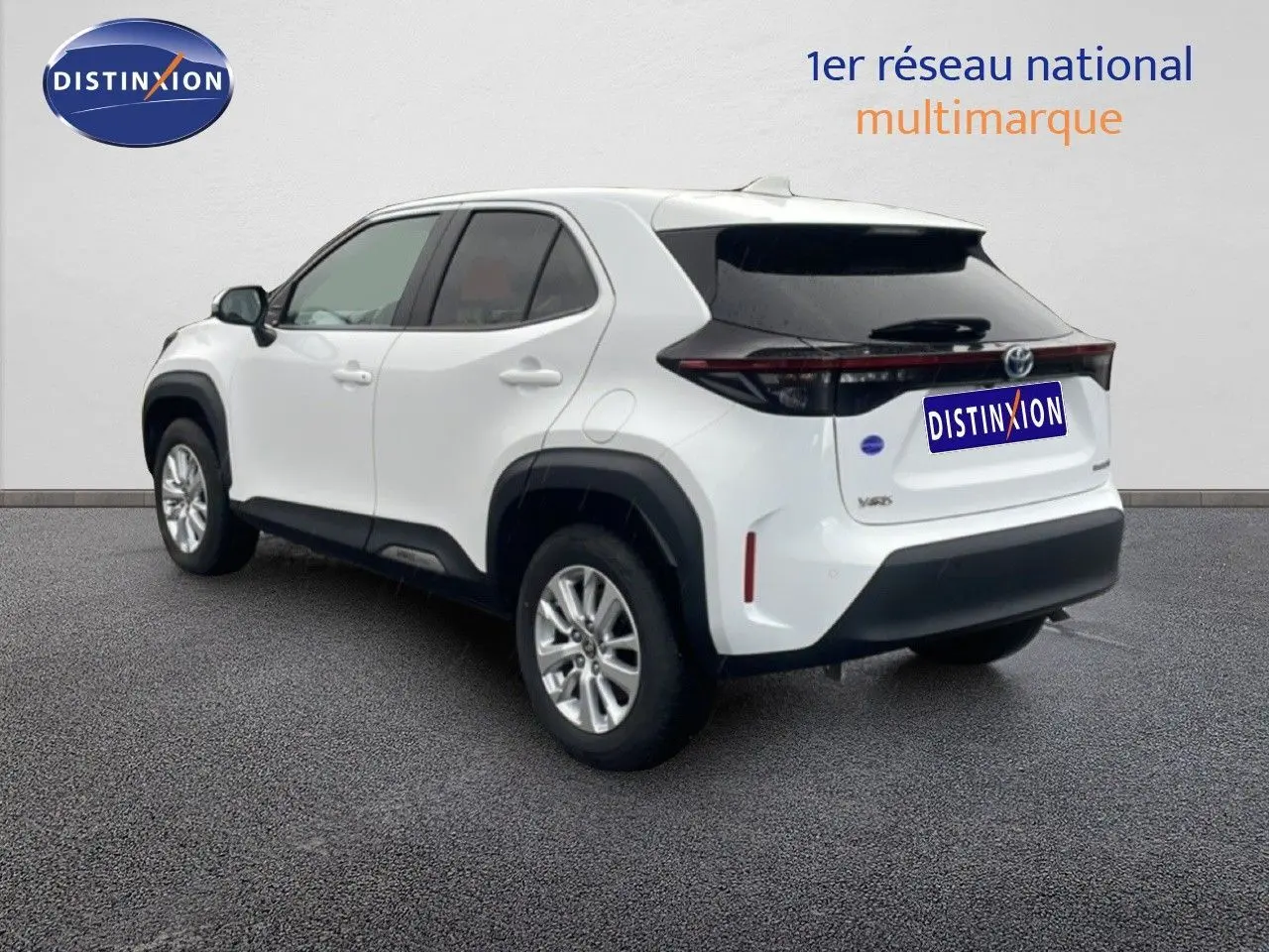 Vue 3/4 arrière droite d'une Toyota Yaris Cross blanche hybride 2024 avec vitres teintées et protections noires.