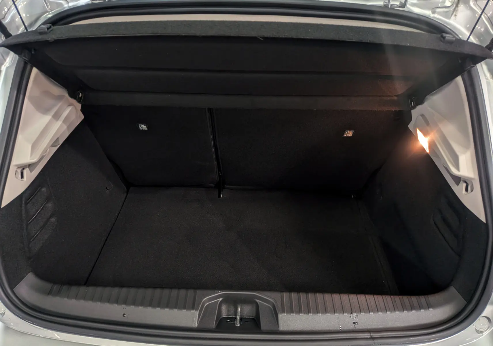 Coffre ouvert vu de l'arrière d'une Renault Clio V gris platine, intérieur noir avec éclairage latéral droit.