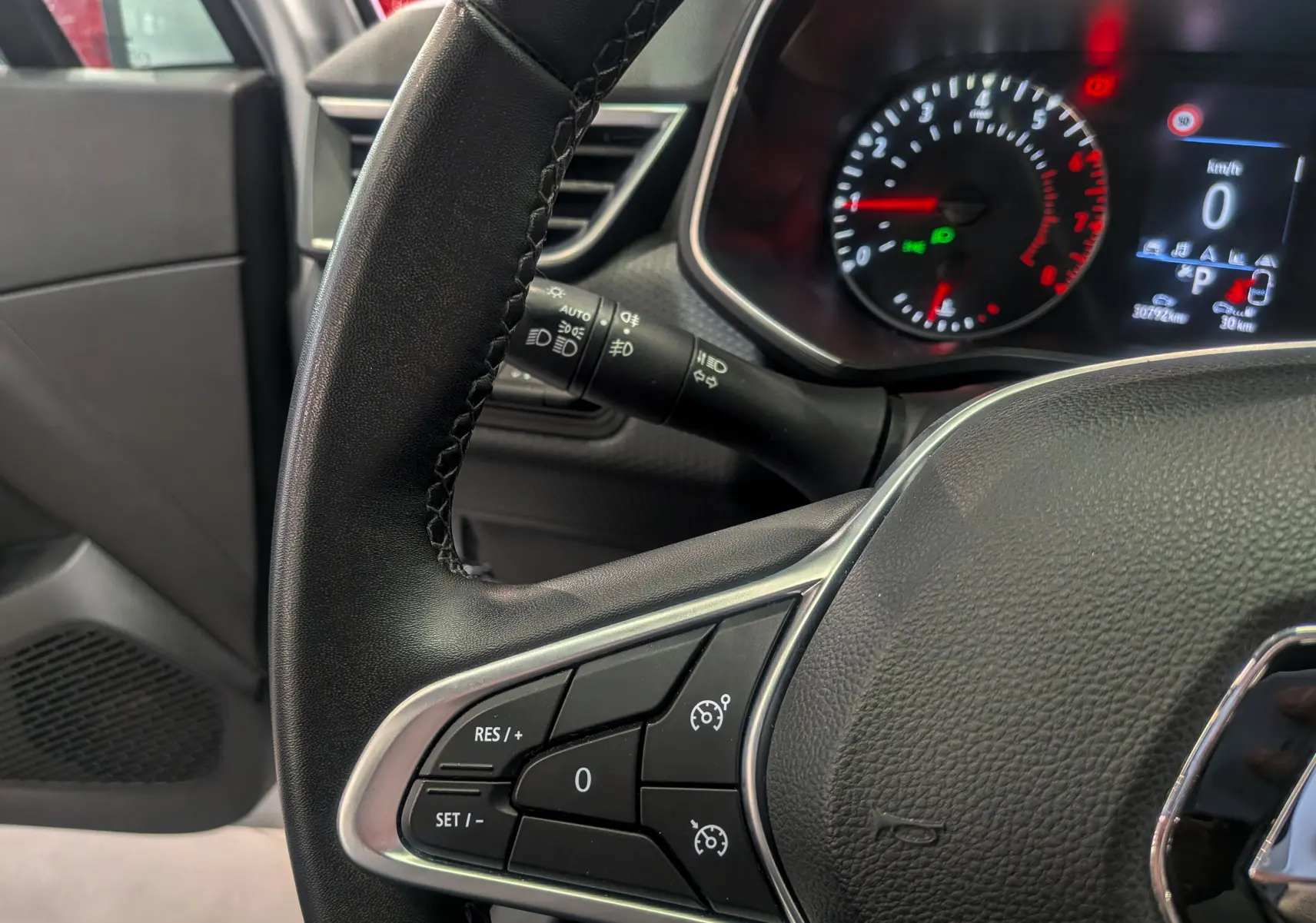 Gros plan sur le volant noir de la Renault Clio V gris platine, avec commandes de régulateur et tableau de bord partiellement visible.