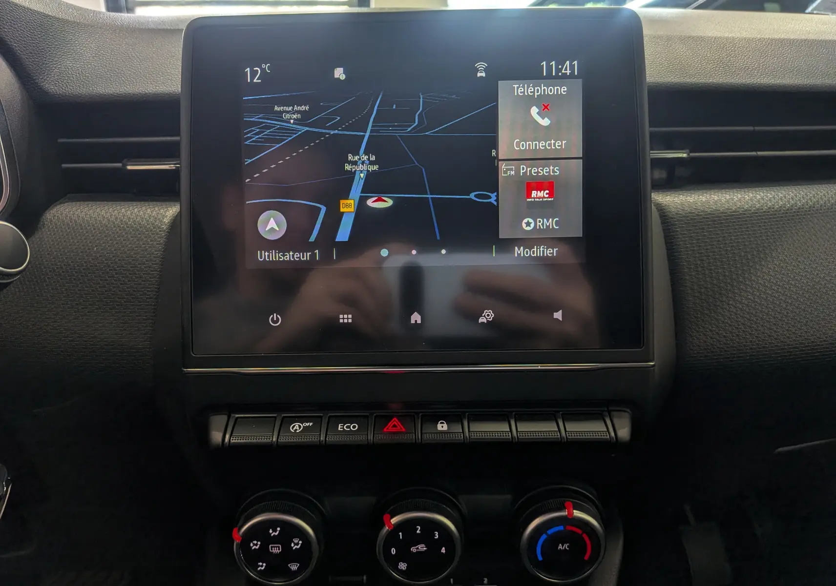 Écran tactile central de la Renault Clio V TCe 90 Auto-école, affichant navigation et commandes climatisation en vue frontale.